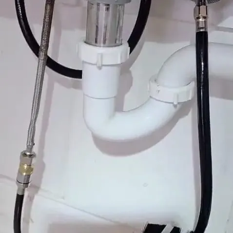 A rebuilt white PVC P-trap and disposal connection under a kitchen sink