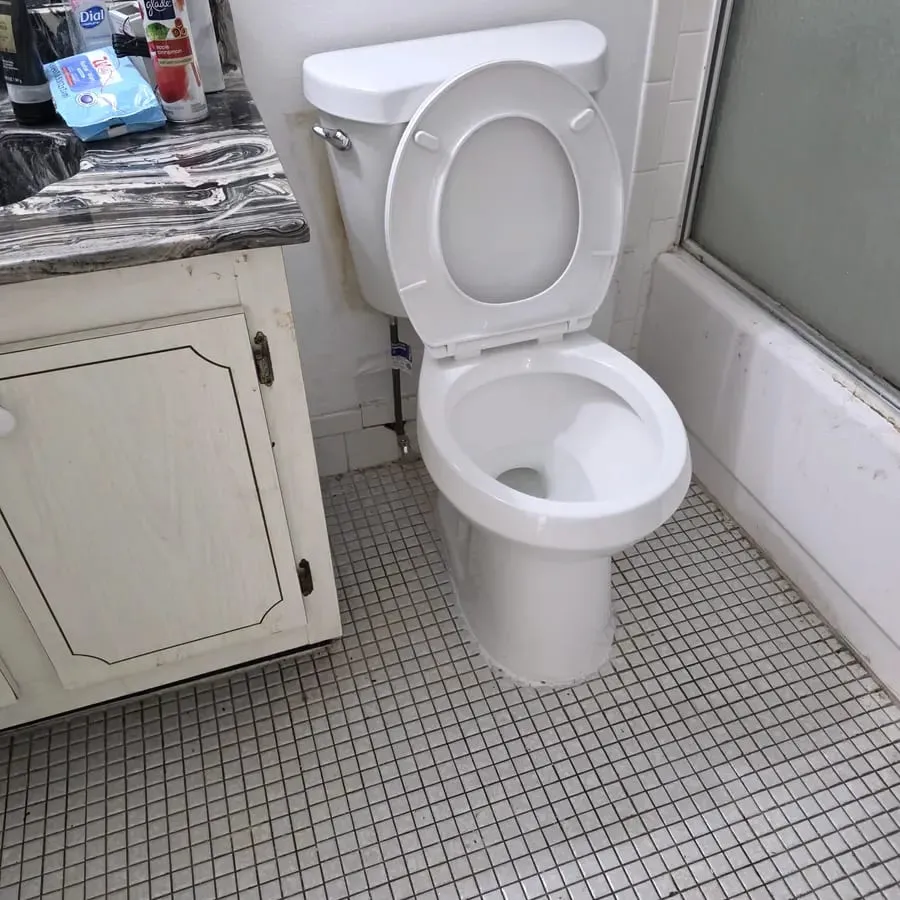 A toilet reset onto a tiled bathroom floor with the vanity and shower enclosure behind it